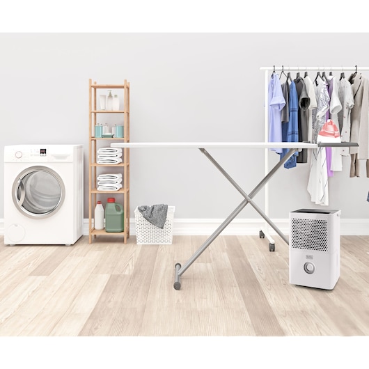 BLACKDECKER BXDH12E dehumidifier front angle in laundry room with washing machine, shelf, and hanging clothes.