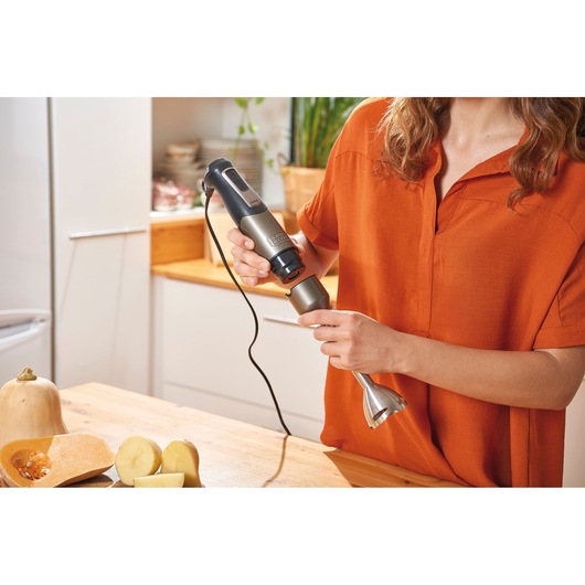 BLACKDECKER BXHBA1000E hand blender in kitchen, woman attaching blending shaft, vegetables on wooden table.