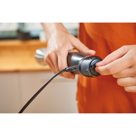BLACKDECKER BXHBA1000E hand adjusting speed dial on black hand blender in kitchen.