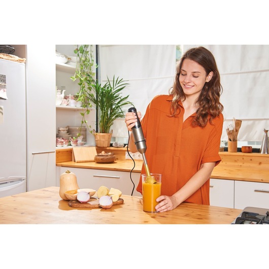 Photo of BLACKDECKER BXHBA1000E hand blender blending orange soup in a glass in a kitchen setting.