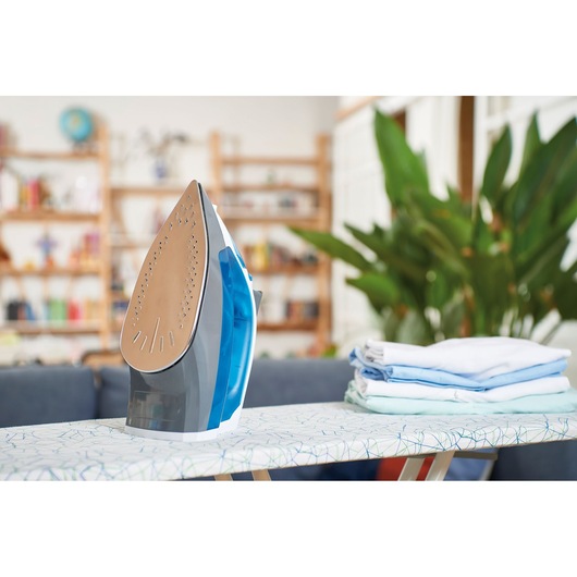 BLACKDECKER BXIR2200E steam iron with blue water tank on ironing board beside folded clothes.