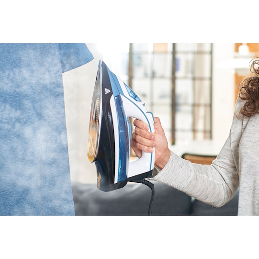 BLACKDECKER BXIR2400E steam iron in use, blue and white, steaming a blue shirt indoors.