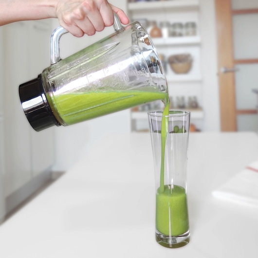 BLACKDECKER BXJB1000E glass blender pouring green smoothie into tall glass on kitchen counter.