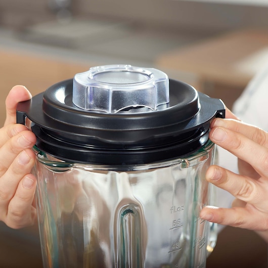BLACKDECKER BXJB1200E blender glass jar with black lid and clear cap held by hands, close-up.