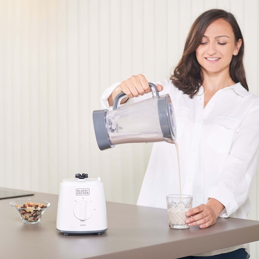 Photo of BLACK+DECKER BXJB500E blender in white on kitchen counter with woman pouring smoothie from jug into glass.