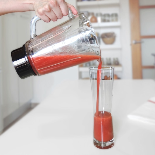BLACKDECKER BXJB800E blender pitcher pouring red smoothie into tall glass in kitchen.