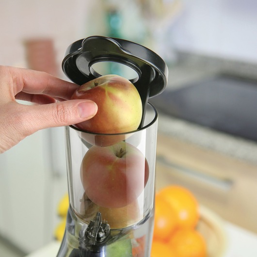 BLACKDECKER BXJE200E juicer chute with whole apples being inserted, kitchen background, close-up.