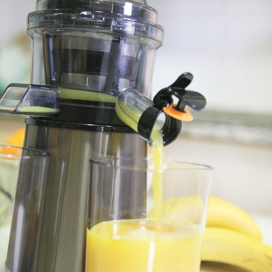 BLACKDECKER BXJE200E juicer in use, yellow juice pouring into glass, kitchen background, product close-up.