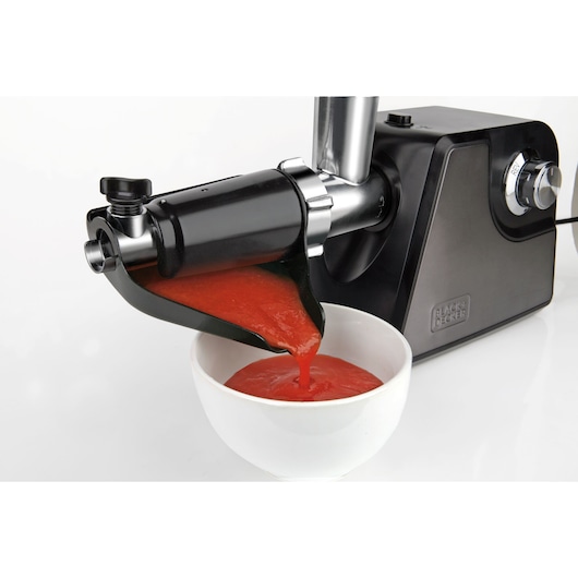 BLACK+DECKER BXMMA1000E electric food mill side view with tomato sauce pouring into white bowl.