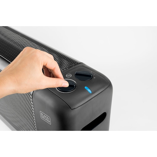 Photo of a hand adjusting control knob on BLACK+DECKER BXMRA1500E black heater, close-up of top panel.