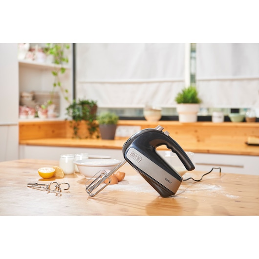 BLACKDECKER BXMX500E handheld mixer in black and silver on a kitchen table with baking ingredients.