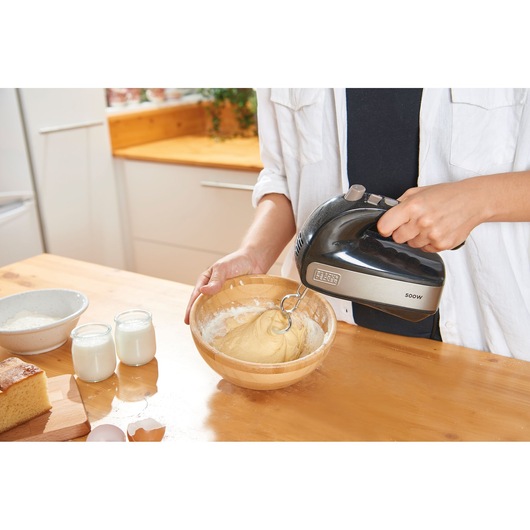 BLACKDECKER BXMX500E hand mixer mixing dough in a wooden bowl on kitchen counter, side angle.