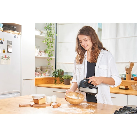 BLACKDECKER BXMX500E hand mixer used to blend ingredients in a wooden bowl on a kitchen counter.