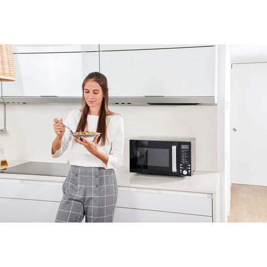 Photo of BLACK+DECKER BXMZ900E microwave in a modern kitchen, person standing beside eating from a bowl.