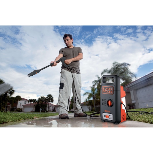 BLACK+DECKER BXPW1300E pressure washer used outdoors on driveway, compact black and orange design shown.
