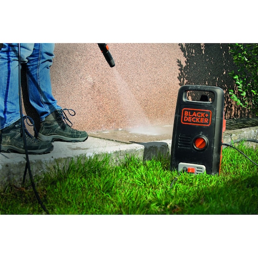 BLACK+DECKER BXPW1300PE pressure washer in use cleaning outdoor concrete surface, close-up view.