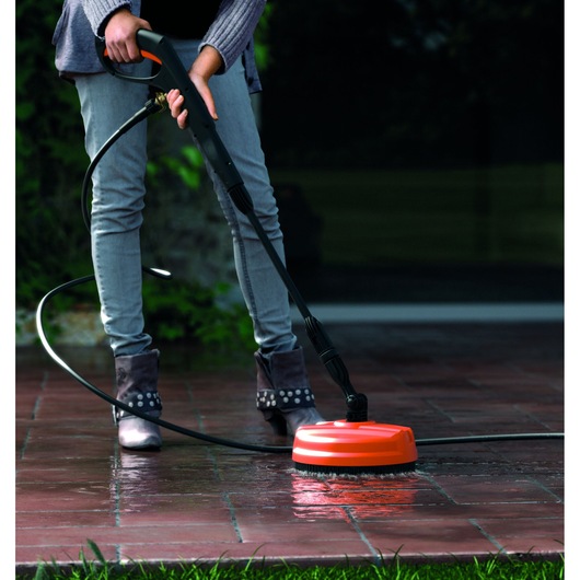 BLACKDECKER BXPW1400PE pressure washer being used to clean outdoor tiles with orange surface attachment.