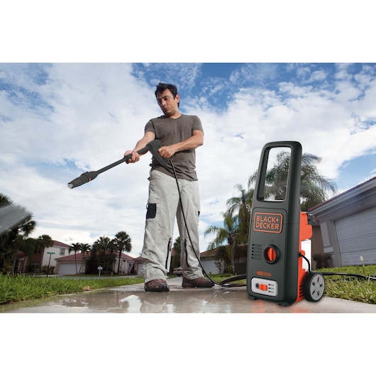 BLACK+DECKER BXPW1500E pressure washer on driveway with person cleaning outdoor surface.