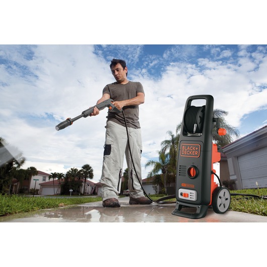 BLACK+DECKER BXPW1700E pressure washer used outdoors on a driveway, black and orange unit with hose.