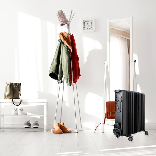 BLACKDECKER BXRA2000E black radiator heater in a modern entryway, near coat rack and mirror.