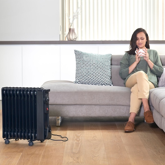 BLACKDECKER BXRA2000E black radiator heater on wheels in living room near sofa.