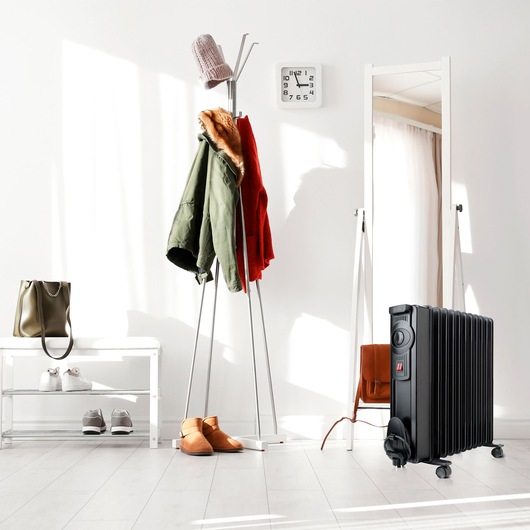 Photo of BLACKDECKER BXRA2300E black oil-filled radiator heater on wheels in modern hallway with coat rack and mirror.