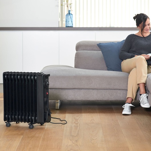BLACKDECKER BXRA2300E black oil-filled radiator heater on wheels in modern living room.