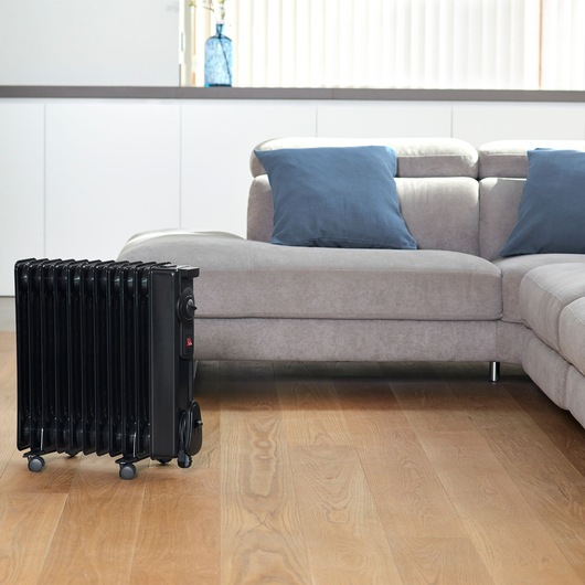 BLACKDECKER BXRA2300E black radiator heater on wheels next to grey sofa in living room.
