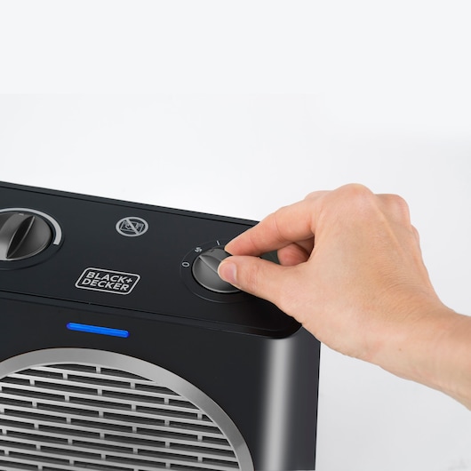 Photo of a hand adjusting the control knob on a BLACK+DECKER BXSH2003E black electric heater, close-up.