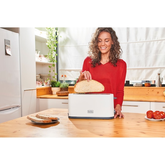 BLACK+DECKER BXTO1001E toaster on kitchen counter with person placing bread slice inside.