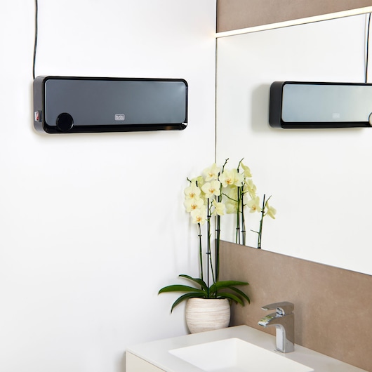 Photo of BLACK+DECKER BXWSH2000E wall-mounted heater in a modern bathroom above a sink with a potted orchid plant.
