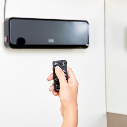 BLACKDECKER BXWSH2000E wall-mounted heater with remote control, close-up hand operating device.