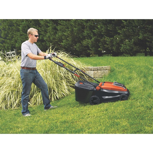 BLACKDECKER CLM3820L1 cordless lawn mower, orange and black, in use on green grass outdoors.