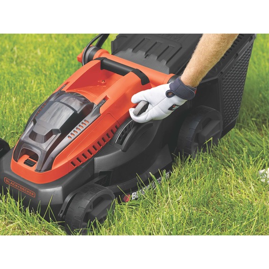 BLACKDECKER CLM3820L1 lawn mower in orange and black, side angle, shown on grass with a gloved hand adjusting lever.