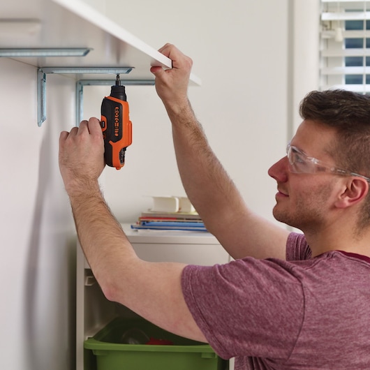 Photo of BLACK+DECKER CS36BSCES cordless screwdriver in use, fastening a screw into a wall shelf bracket.