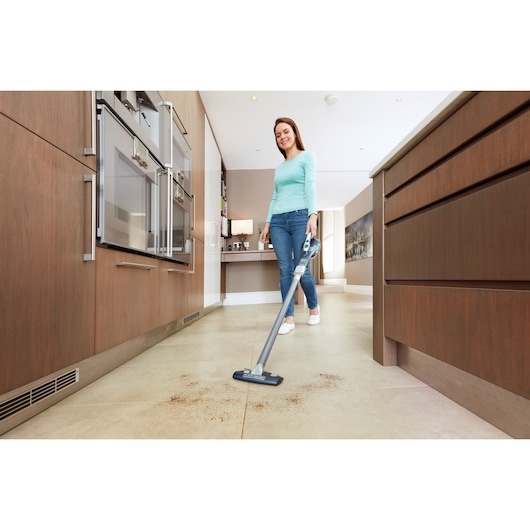 BLACKDECKER DVA315JF cordless stick vacuum cleaning kitchen floor with dust visible, in use by person.