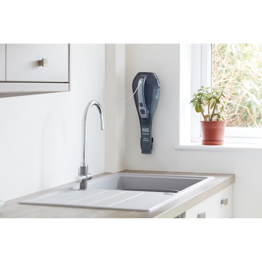 BLACKDECKER DVA315JF handheld vacuum mounted on kitchen wall near sink and potted plant, front angle.