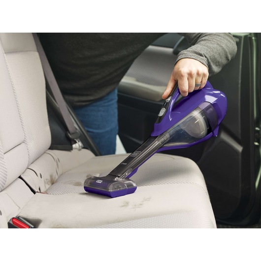 BLACK+DECKER DVA325JP07 handheld vacuum in purple used to clean a car seat, side angle.