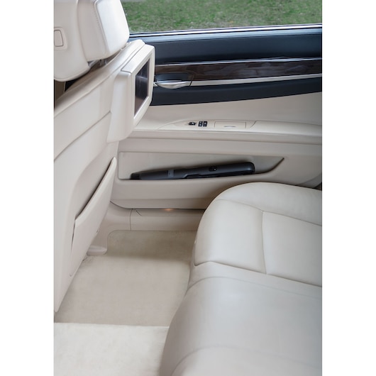 A BLACK+DECKER handheld vacuum cleaner placed inside the door compartment of a beige car interior.