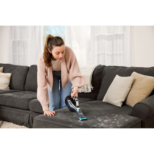 BLACKDECKER DVD320B handheld vacuum cleaning pet hair from dark sofa in living room.