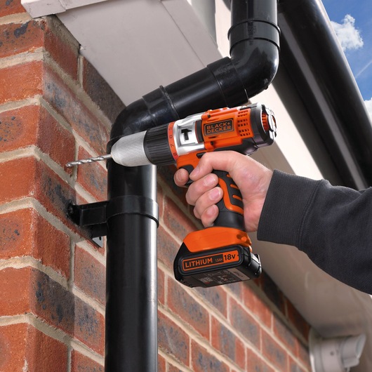 BLACKDECKER EGBHP1881K cordless drill used to drill into exterior brick wall, lithium 18V battery visible.