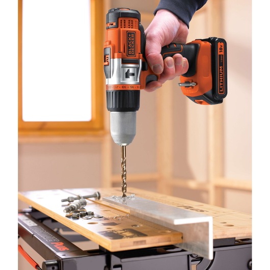 BLACKDECKER EGBHP1881K cordless drill in use, drilling into metal on a workbench, close-up angle.