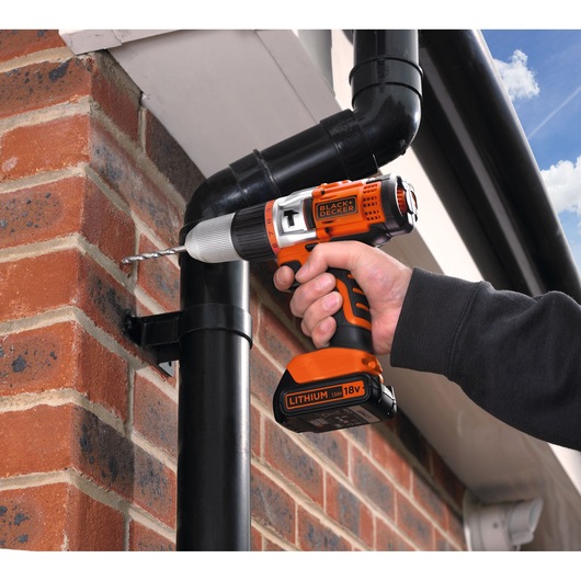 BLACKDECKER EGBHP1881K cordless drill in use, orange and black, drilling into brick wall outdoors.