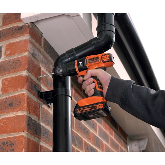 Photo of BLACKDECKER EGBL188KB cordless drill, orange and black, used to drill into outdoor brick wall.