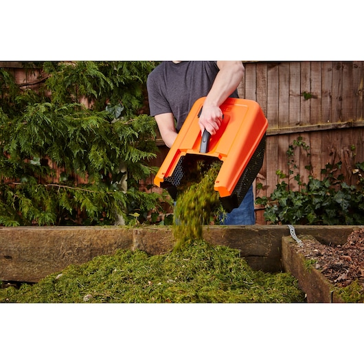 BLACKDECKER EMAX32S lawn mower grass box being emptied onto compost heap outdoors.