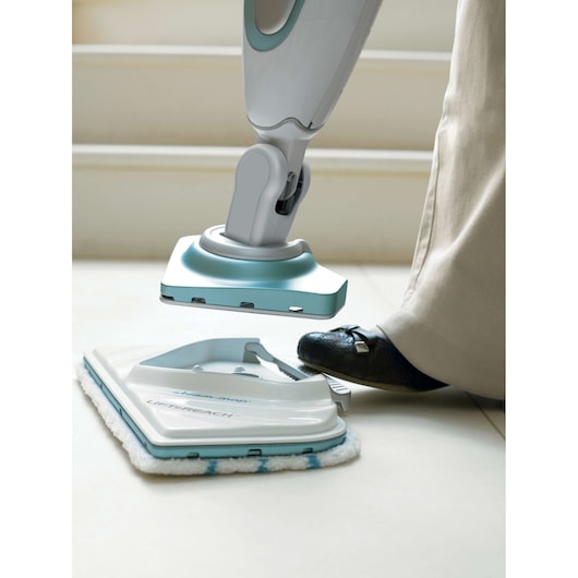 Photo of BLACKDECKER FSM1616 steam mop head being attached by foot, white background, cleaning pad visible.