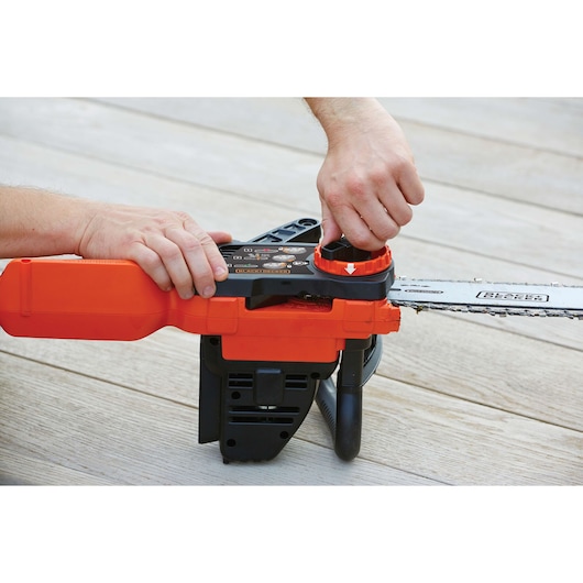 Close-up of a person adjusting the chain tension on an orange and black cordless chainsaw placed on a wooden surface.