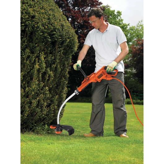 BLACKDECKER GL7033CAKIT orange electric grass trimmer in use outdoors on lawn near bushes.