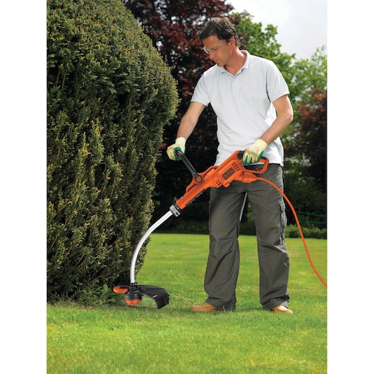BLACKDECKER GL8033 grass trimmer used outdoors by person trimming lawn edge near hedge.