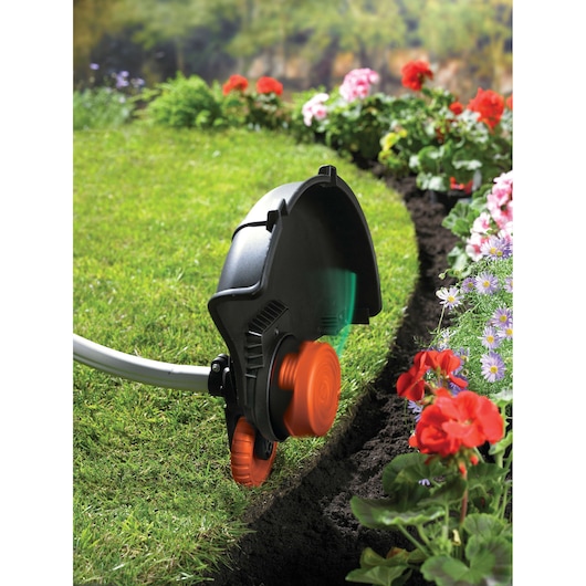 BLACKDECKER GL9035 grass trimmer with orange wheel trim edge cutting along lawn and flower bed.